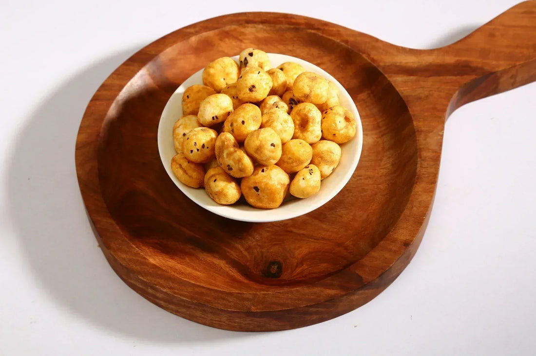 Close-up of a white bowl filled with roasted and seasoned popped water lily seeds(makhana) placed on a wooden serving board.